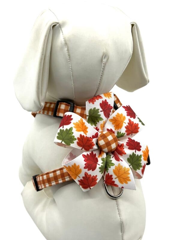 A white dog wearing a Burnt Orange Check w/ Optional Bow Choices- "H" Style Harness with fall leaves.