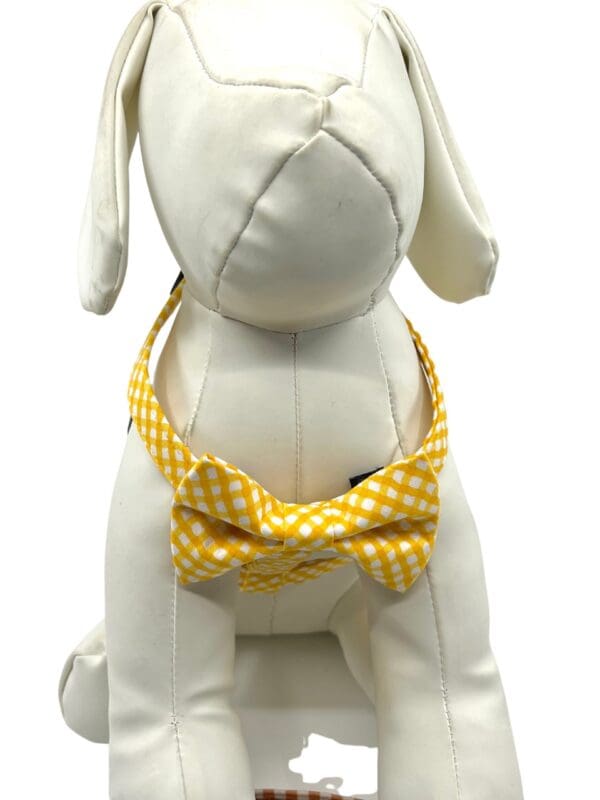 A white dog wearing the Yellow Gold Check- "H" Style Harness w/Bow Tie.