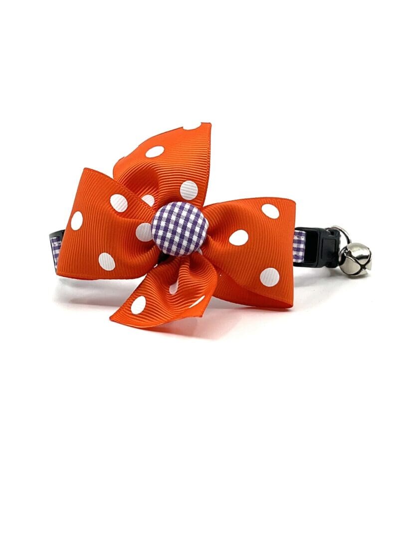 An orange and white polka dot cat collar with a bell.