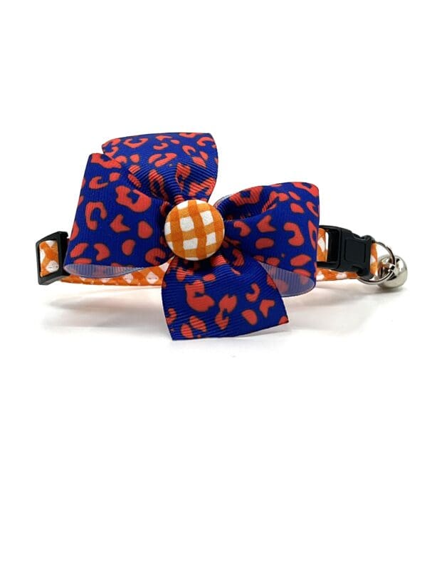A cat collar with an orange and blue bow.