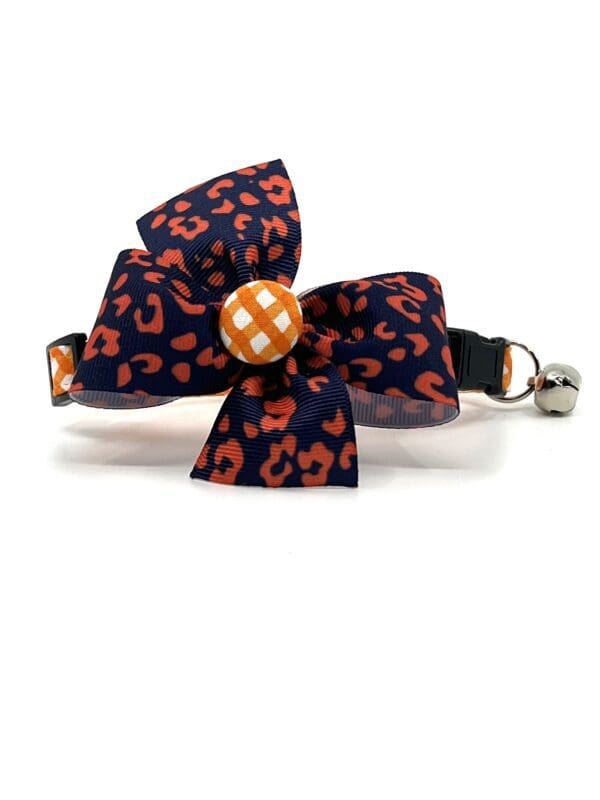 A cat collar with an orange and blue bow.