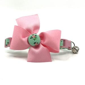 A pink cat collar with a pink bow on it.