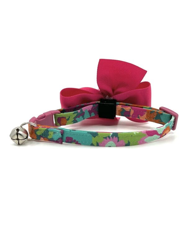 A cat collar with a bow and bell on it.