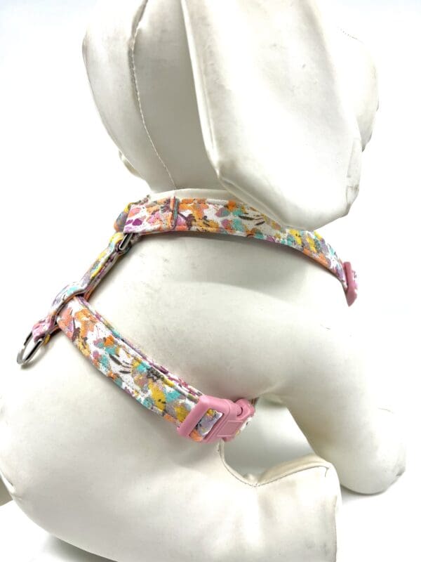 A white dog wearing a pink floral harness.