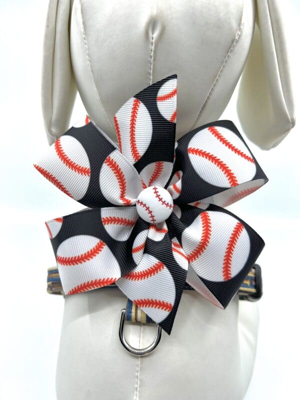 A dog 's harness with baseball ribbon flower.