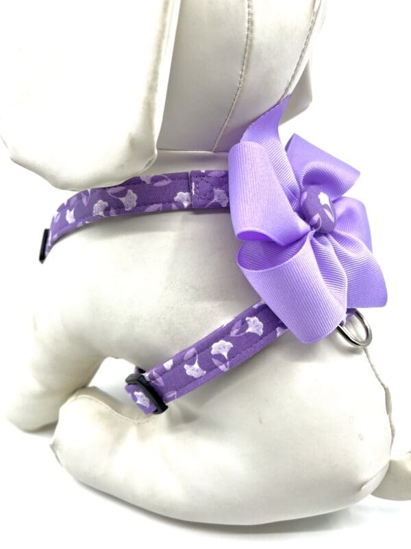 A dog wearing a purple bow on its harness.