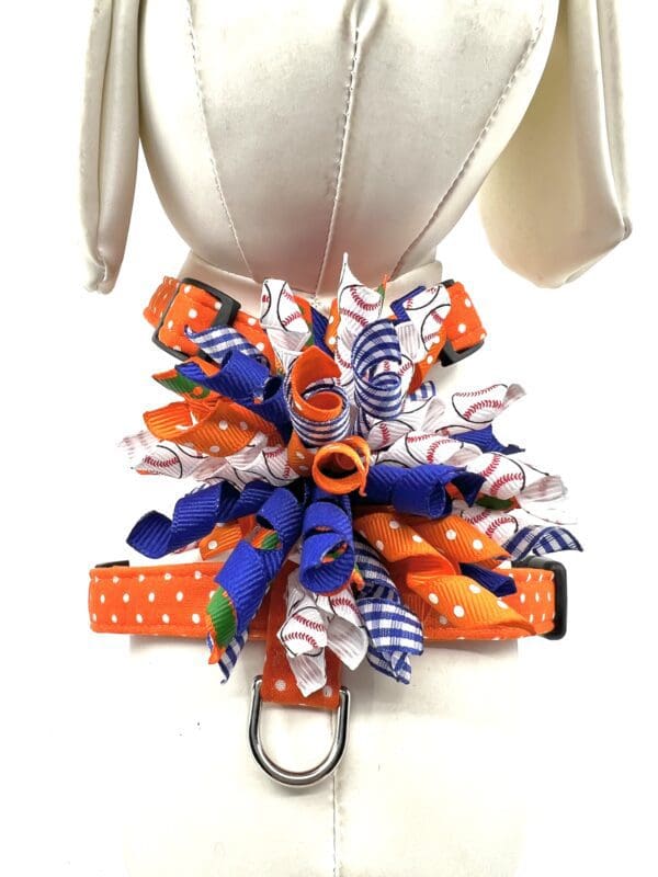 A dog harness with an orange and blue bow.