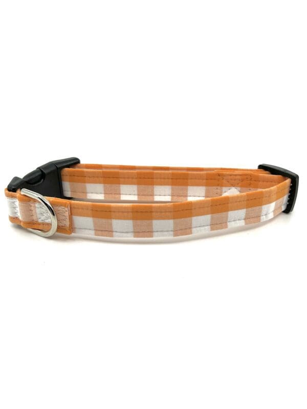 A dog collar that has an orange and white plaid pattern.