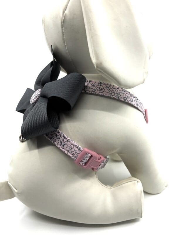 A small dog wearing a harness with a bow.
