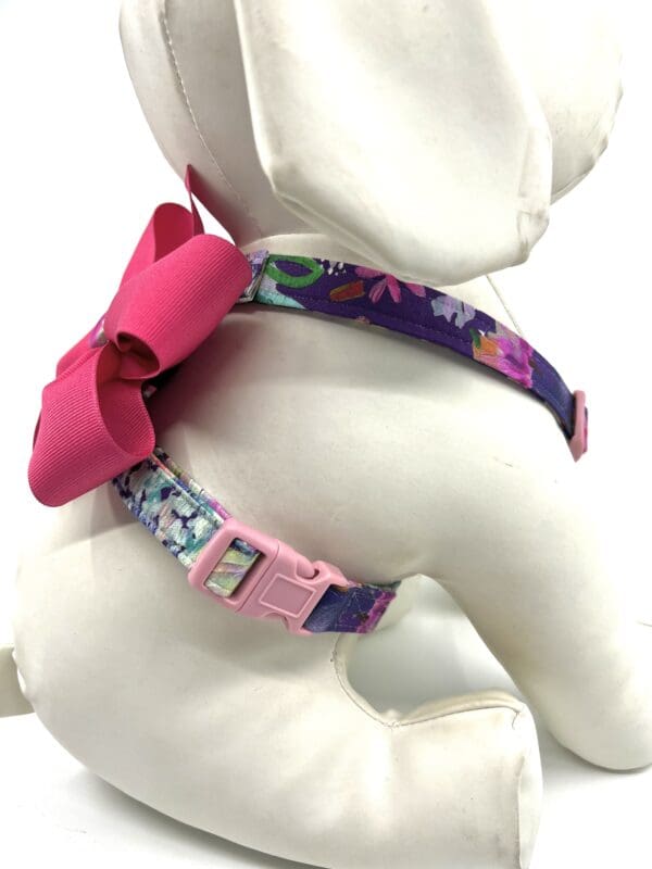 A stuffed teddy bear wearing a floral dog harness.