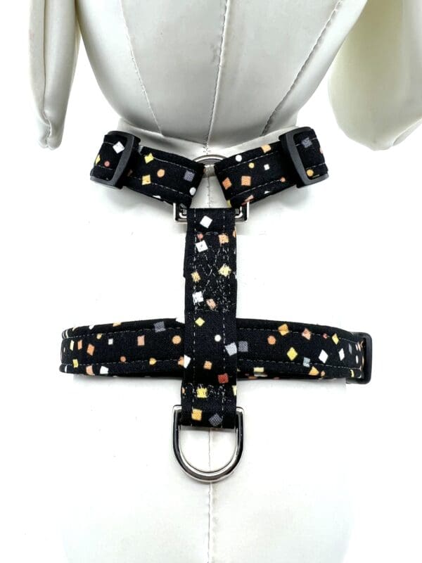 A black dog harness with multi colored polka dots.