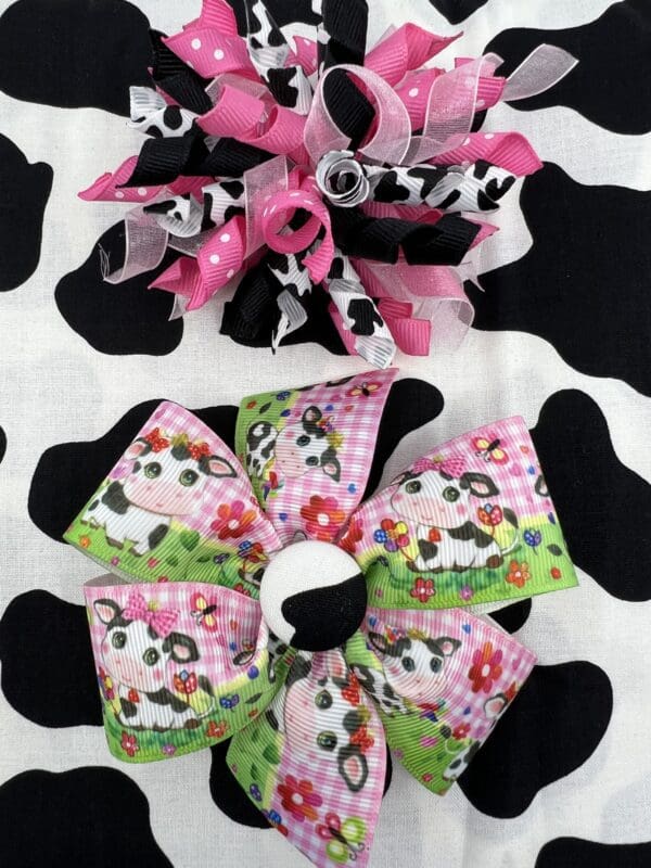 Two bows of different colors on a cow print background.