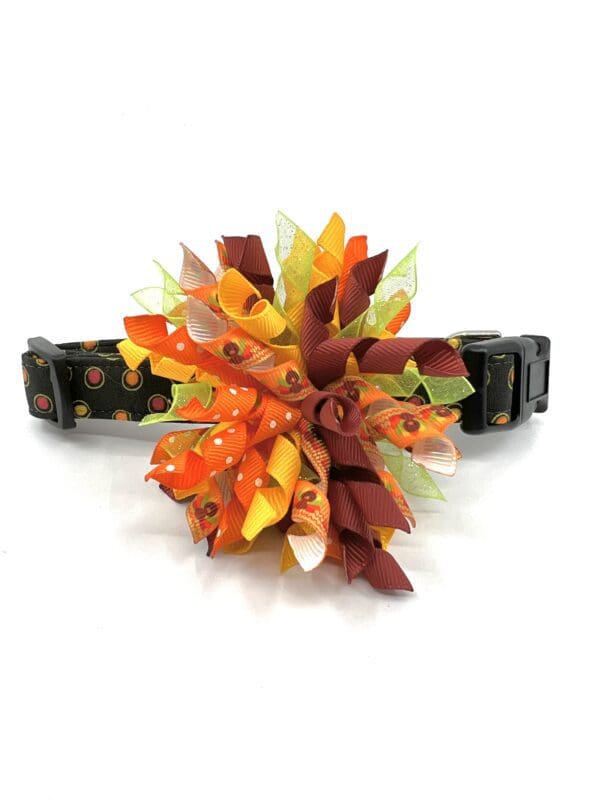 A dog collar with an orange and yellow pom pom.