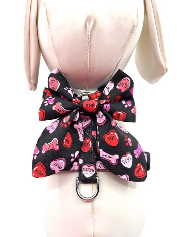 A black dog harness with hearts and bows on it.