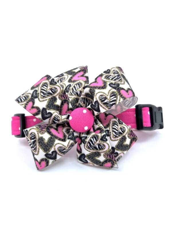 A pink and black cat collar with a bow on it.